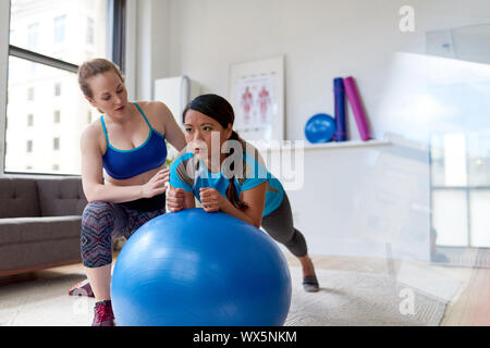 Kaukasische Frau Physiotherapeutin ein Training Session eine Zwischenbilanz nach chinesischen weiblichen Patienten auf einem Gymnastikball Stockfoto