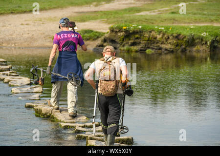 OGMORE VON MEER, WALES - April 2019: Zwei Personen mit Metalldetektoren gehen auf Trittsteine über den Fluss Ogwr in Ogmore vom Meer in South Wales Stockfoto