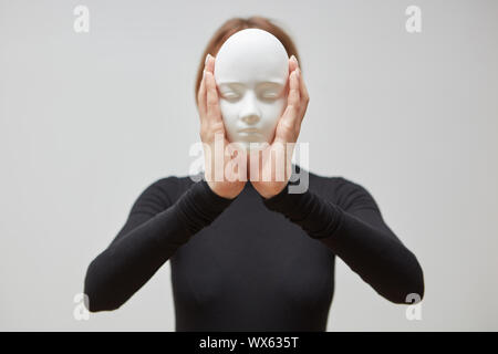 Attraktive Mädchen in einer Steckbrücke schwarz hält Gips Maske Skulptur statt Gesicht auf einem weißen Hintergrund. Konzept Die Masken die Wir tragen Stockfoto