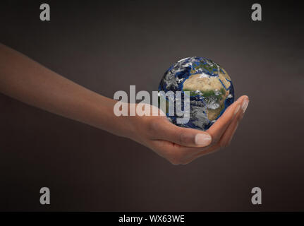 Weibliche Hand, die die Erde gegen einen dunklen Hintergrund Stockfoto