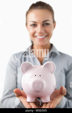 Nahaufnahme von piggy Bank durch lächelnd weibliche Bank assistant vor einem weißen Hintergrund gehalten wird Stockfoto