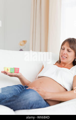 Gute Suche schwangere Frau spielen mit Holz unterbauen und das Wort 'Junge' auf ihre Hand geschrieben, während auf einem Sofa liegend Stockfoto