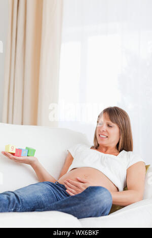 Attraktive schwangere Frau spielen mit Holz unterbauen und das Wort "Mädchen" auf die Hand geschrieben, während auf einem Sofa liegend Stockfoto