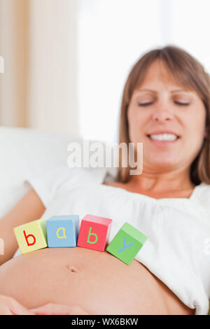 Attraktive schwangere Frau spielen mit Holz unterbauen, während auf einem Sofa in Ihrem Wohnzimmer liegend Stockfoto