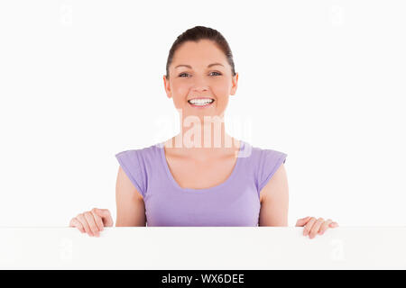 Porträt einer charmanten Frau posiert hinter einer Anschlagtafel beim Stehen vor einem weißen Hintergrund Stockfoto