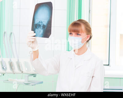 Junge Frau in Schutzmaske dotstor schaut auf eine Röntgenaufnahme des Schädels Stockfoto