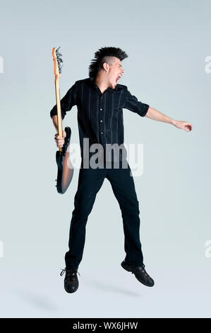 Genial Mohawk Mann springt mit seiner Gitarre im studio Stockfoto