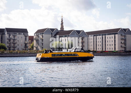 Ein Hafen-Bus wird in Wohnblocks in Christianshavn, Kopenhagen, Dänemark. Die Turmspitze Vor Frelsers Kirke, Kirche unseres Erlösers, in der Ferne Stockfoto