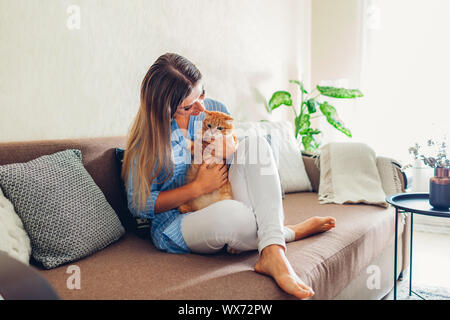 Spielen mit der Katze zu Hause. Junge Frau sitzt auf der Couch und Umarmen pet. Stockfoto