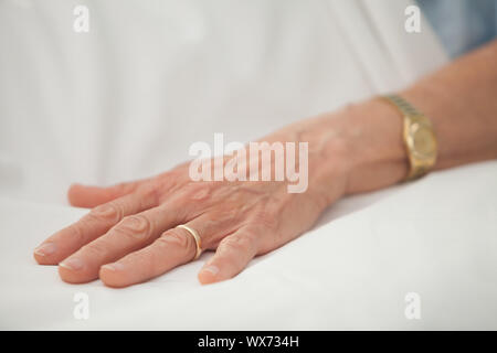 Hand einer alten Frau mit Goldschmuck im Krankenhausbett Stockfoto