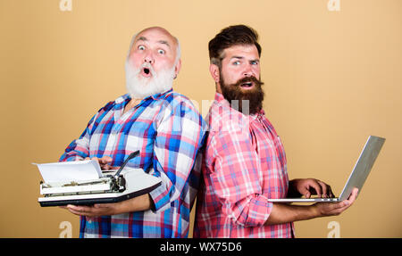 Retro Schreibmaschine vs Laptop. Neue Technologie generation. Technologie Schlacht. Modernes Leben. Jugend vs Alter. business Ansatz. Zwei bärtigen Männern. Vintage Schreibmaschine. Vater und Sohn. Master neue Technologie. Stockfoto