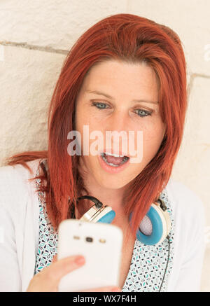 Ausdrucksstarkes portrait einer hübschen rothaarigen Frau liest die Informationen auf Ihrem Mobiltelefon Stockfoto