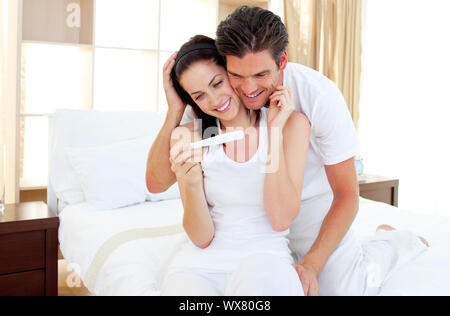 Verliebten Paar herauszufinden, Ergebnisse einer Schwangerschaft testen auf dem Bett sitzt Stockfoto