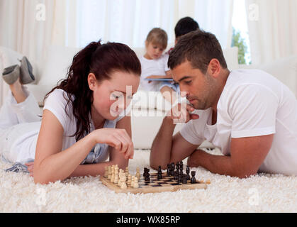 Eltern Schach spielen auf dem Fußboden im Wohnzimmer, mit Ihren Kindern auf dem Sofa Stockfoto