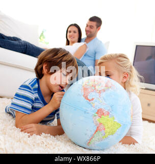 Kinder spielen mit einer Erdkugel im Wohnzimmer mit ihren Eltern auf dem Sofa Stockfoto