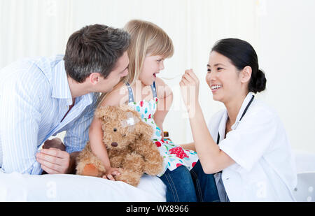 Professionelle female Arzt, der Sirup zu einem netten kleinen Mädchen gegen weißen Hintergrund Stockfoto