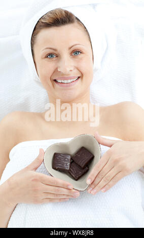 Fröhliche Frau mit einer Schüssel in der Form eines Herzens mit Schokolade in einem Wellnesscenter Stockfoto