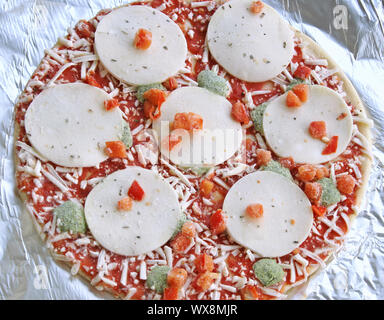 Gefrorene dünne Kruste Pizza mit Mozzarella Käse und Gemüse auf Alufolie bereit zum Kochen Stockfoto