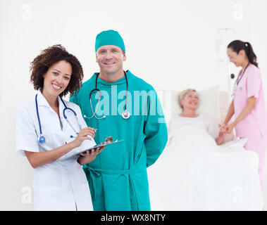 Charismatische Team von Ärzten an Kamera Patienten in ihrem Bett liegend lächelnd Stockfoto