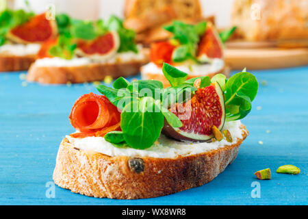 Toast von Schweizer twisted Brot, mit Feta oder Ricotta, frische Feigen, gerollt Scheibe Speck, frische Blätter von Mais oder baldrian Salat und zerdrückten Pis Stockfoto