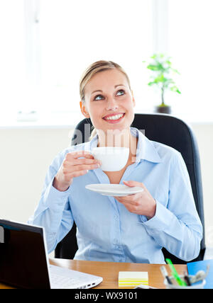 Freuen Geschäftsfrau trinken Kaffee vor Ihrem Laptop in Ihrem Büro an ihrem Schreibtisch Stockfoto