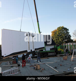 Handwerker in einem vorgefertigten Wand, die von einem Kran hängt, wie es zu einer Baustelle zur Installation auf der Zement geliefert wird Stockfoto