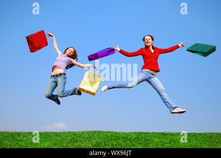 Mädchen springen mit Taschen gegen den blauen Himmel Stockfoto