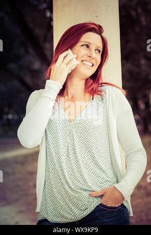 Hübsches Lächeln rothaarige Frau, die einen Anruf mit Ihrem Handy in einem Park. Jahrgang Behandlung Stockfoto