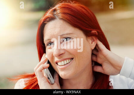 Portrait von lächelnden schöne junge Frau in der Nähe von Mobiltelefon, gegen den Hintergrund der Sommer Green Park. Stockfoto