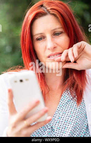 Portrait von lächelnden schöne junge Frau in der Nähe von Mobiltelefon, gegen den Hintergrund der Sommer Green Park. Stockfoto
