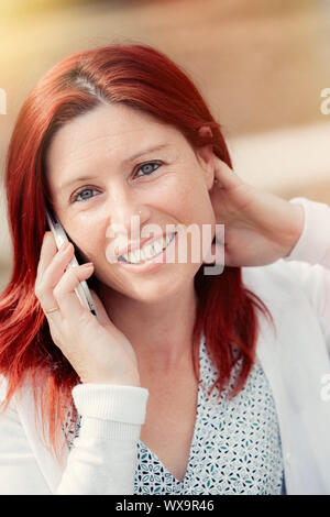 Portrait von lächelnden schöne junge Frau auf einer Bank sitzen mit Handy, gegen den Hintergrund der Sommer Green Park. Stockfoto