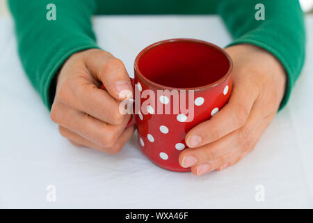 Frau mit einer roten Kaffeetasse mit weißen Tupfen auf einem weißen Tischtuch Stockfoto