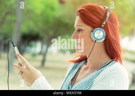 Porträt eines attraktiven Lächeln rothaarige Frau hören die Musik auf Ihrem Telefon mit einem Headset mit dem Grün im Hintergrund Stockfoto