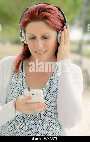 Porträt eines attraktiven Lächeln rothaarige Frau hören die Musik auf Ihrem Telefon mit einem Headset mit dem Grün im Hintergrund Stockfoto