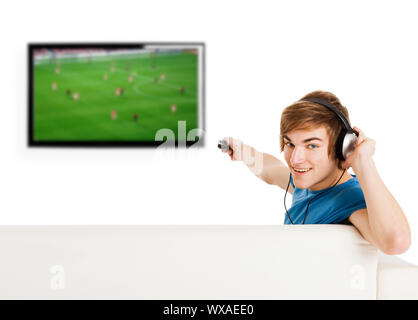Junger Mann sitzt auf der Couch mit einer Fernbedienung und ein Fußballspiel im Fernsehen anschauen Stockfoto