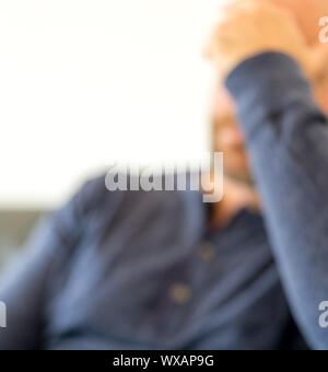 Aus Mann in den Vierzigern sitzen auf der Couch mit dem Kopf in seiner Hand verbrannt Defokussierten Stockfoto