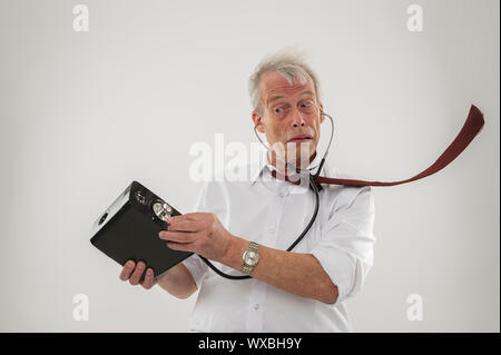 Konzeptionelle studio Schuß über weiß von einem alten Mann mit ein Hörproblem, der mit einem Stethoskop, um zu versuchen, seine Audio Lautsprecher hören Stockfoto