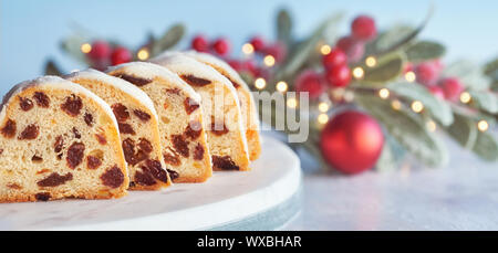 Christstollen auf Weiß-Blau festliche Hintergrund mit Beeren und Weihnachtsbeleuchtung. Traditionelle deutsche Dessert für Weihnachtsfeier, Panorama compo Stockfoto