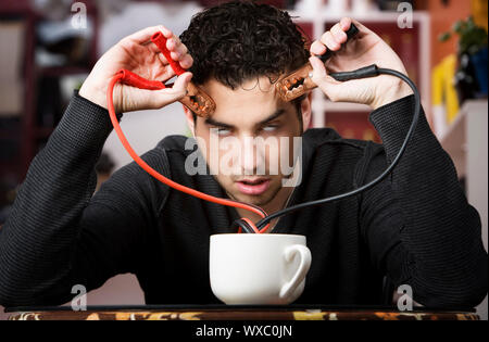 Junger Mann Betrieb Starthilfekabel aus der Kaffeetasse Stockfoto