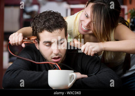 Junge Frau mit Starthilfekabel aus Kaffeetasse kommen zum Kopf des Mannes Stockfoto