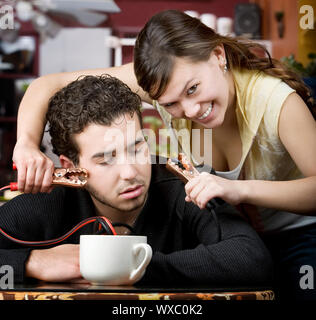 Junge Frau mit Starthilfekabel aus Kaffeetasse kommen zum Kopf des Mannes Stockfoto