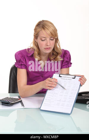 Blonde Büroangestellte zeigt auf Clip-Board mit Stift Stockfoto