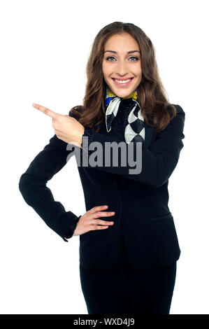 Freundlich lächelnde Stewardess entfernt zeigen und posiert in Stil mit einer Hand auf Taille. Stockfoto