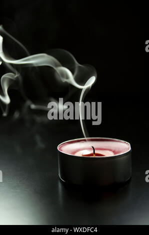 Eine rote Kerze auf einem Schwarzen Tisch ist zu rauchen, nachdem es gelöscht ist. Stockfoto