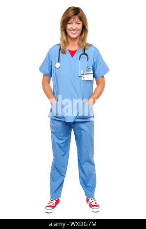 In voller Länge Portrait von blonde Arzt in einheitlichen posiert mit Hände in der Tasche. Stockfoto