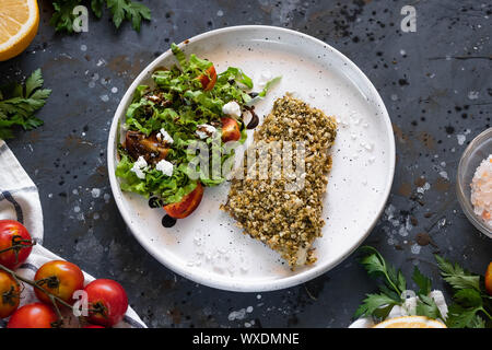 Gebackener Wolfsbarsch würzigen Panade mit frischen Salat. Ein Beispiel für ein ausgewogenes Mittagessen. Das Konzept der richtige Ernährung. Leckere, gesunde und einfache Gerichte. Stockfoto