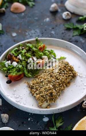 Gebackener Wolfsbarsch würzigen Panade mit frischen Salat. Ein Beispiel für ein ausgewogenes Mittagessen. Das Konzept der richtige Ernährung. Leckere, gesunde und einfache Gerichte. Stockfoto