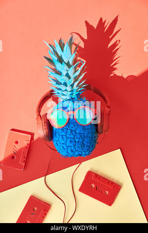 Lustige Ananas in Sonnenbrille und Kopfhörer mit retro Tonbänder. Flach auf Coral Farbe, orange und rot Papier Hintergrund mit Schatten. Stockfoto