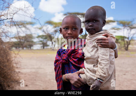 Masai Dorf, Tansania, Afrika - Dezember 11: Zwei Masai Kinder benannt und Kapalei Isina zusammen. Isina trägt das Kind ihrer Eltern helfen auf Stockfoto