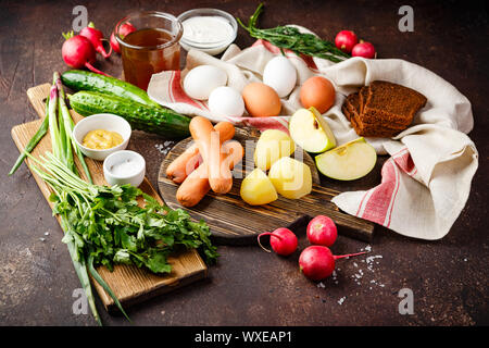 Prozess der Herstellung Okroshka Suppe. Häckseln, Rettich, Wurst und andere Zutaten auf Holz Schneidebrett Stockfoto